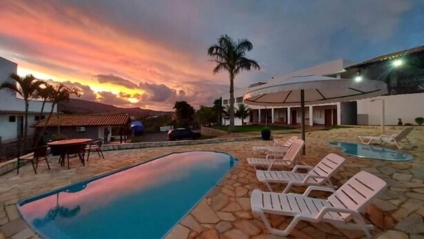Piscina com espreguiçadeiras, área de estar e vista para o pôr do sol.