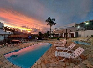 Piscina con sillones de descanso, zona de patio y vista al atardecer.