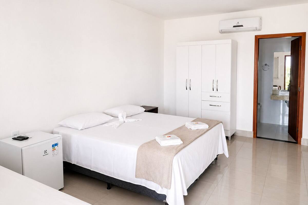 Habitación de hotel con cama, armario, escritorio y un refrigerador pequeño.