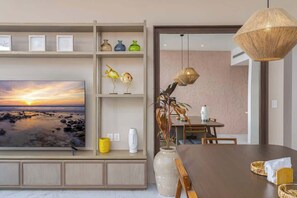 Ein modernes Wohnzimmer mit großem Fernseher, Essbereich und einer Zierpflanze.