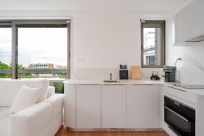 A modern kitchen with white cabinetry, a built-in oven, and a window overlooking a cityscape. - Elysee's Residence / Luxury 1 Bed Serviced Apartment (Paris)