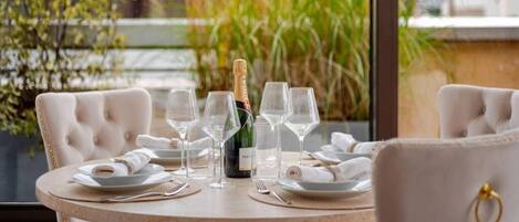 A round dining table with six wine glasses, a bottle of champagne, and folded white napkins.