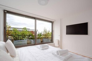 Une chambre dotée d’une grande porte-fenêtre coulissante, d’un lit avec du linge de lit blanc et d’un téléviseur noir fixé au mur.