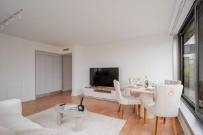 Un salon moderne doté d’un téléviseur à écran plat, d’une table à manger avec des chaises et d’une grande fenêtre.