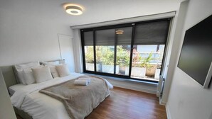 Ein modernes Schlafzimmer mit einem großen Bett, Blick auf Grünfläche draußen und einem Flachbildfernseher an der Wand.
