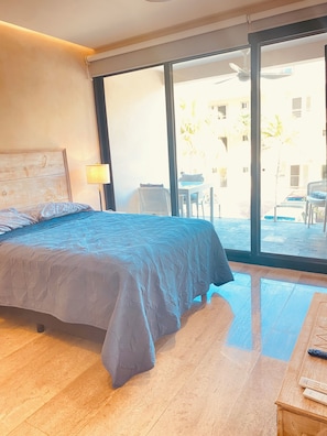 A bedroom with a large bed, a nightstand, a lamp, and a view of the outside. - Condo with kitchen, washing machine, Wi-Fi, drinking water, pool, golf course, and beach (Puerto Aventuras)