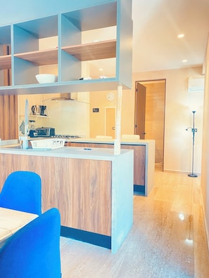 A modern kitchen with a central island, wooden cabinetry, and a dining area with blue chairs. - Condo with kitchen, washing machine, Wi-Fi, drinking water, pool, golf course, and beach (Puerto Aventuras)