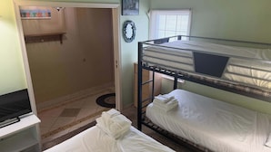 Habitación con literas, un escritorio, una puerta que da a otra habitación y una ventana con persianas.