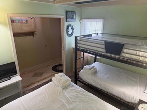 Une chambre avec un lit superposé, un bureau, une porte donnant sur une autre pièce et une fenêtre avec des stores.