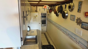 Una cocina estrecha con un lavamanos de acero inoxidable, armarios blancos y salpicadero de azulejos.