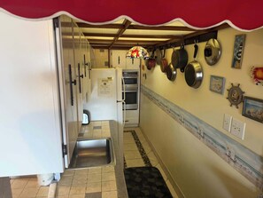 A narrow kitchen with a stainless steel sink, white cabinets, and a tiled backsplash.