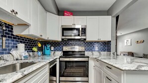 A kitchen with white cabinets, a built-in microwave, a stainless steel oven, and a blue-tiled backsplash. - Sherwood 1C (Ocean City)