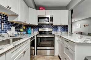 A kitchen with white cabinets, a built-in microwave, a stainless steel oven, and a blue-tiled backsplash. - Sherwood 1C (Ocean City)