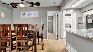 A dining area with wooden chairs and a table, a ceiling fan, and a kitchen with a refrigerator and microwave. - Sherwood 1C (Ocean City)