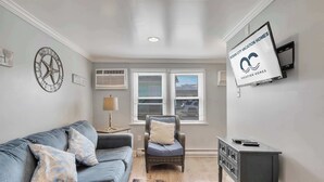 En stue med en grå sofa, en fletstol, et lille bord og et ophængt fjernsyn, der viser 'Ocean City Vacation Homes'.