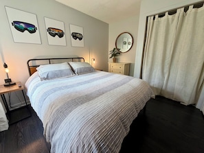 A bedroom with a bed, bedside table with lamp, wall art, dresser, mirror, and curtains. - ShnowFun: Ski-In/Ski-Out & Summer Adventure Condo (Great Valley)