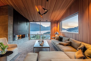 A modern interior with a large window, a fireplace, a sofa, and a coffee table. - Ladena by MajorDomo (Queenstown)
