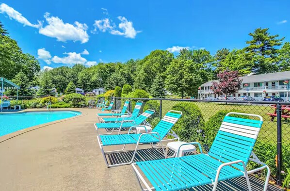 A poolside area with lounge chairs, a swimming pool, and a building with a balcony in the background.