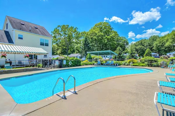 A swimming pool with a covered area, lounge chairs, and a building with a sloped roof.