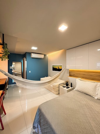 A modern hotel room with a bed, a desk, a chair, a hammock, a nightstand, and an air conditioning unit.. Studio Aconchegante Território Serra da Capivara