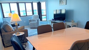 Een woonkamer met een eettafel, stoelen, een bank, een televisie en een lamp.