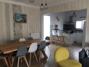 Un coin repas avec une table et des chaises en bois, une cuisine avec des meubles blancs et un tableau accroché au mur.