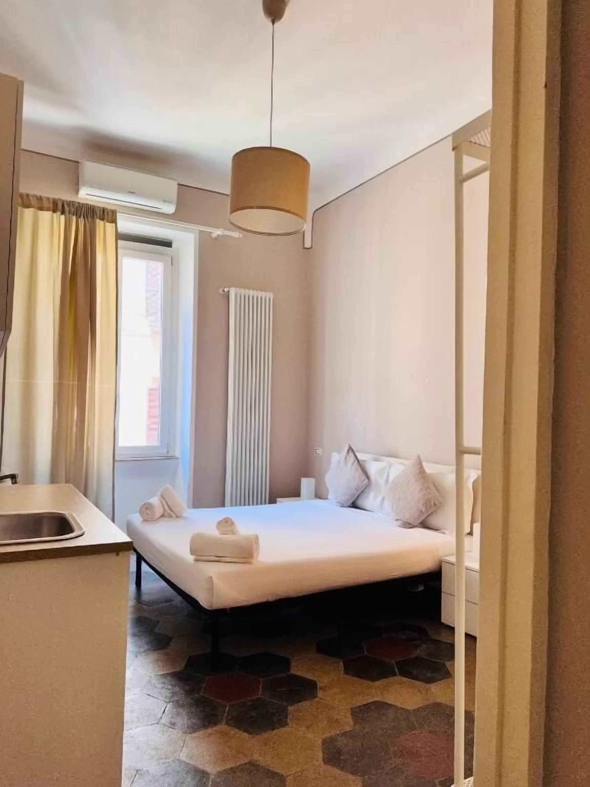 Une chambre d’hôtel avec un lit, un petit bureau, un radiateur et une fenêtre avec des rideaux.