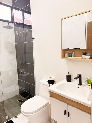 Een moderne badkamer met een douchecabine van glas, een wit toilet, een witte wastafel met een zwarte kraan en een houten wastafelmeubel met een spiegel erboven.