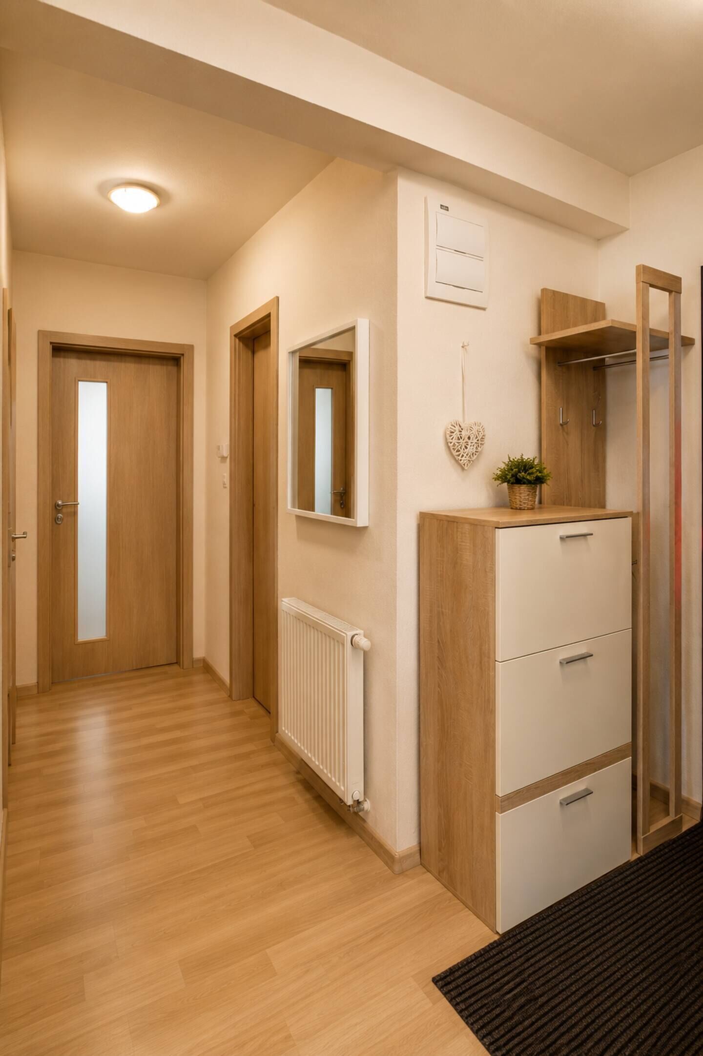 A hallway with wooden flooring, a radiator, a mirror, a heart-shaped decoration, and a wardrobe.