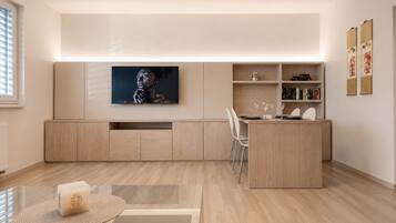 Una cocina moderna con zona de comedor, muebles de madera, un televisor sobre la encimera y una estantería con libros.