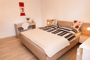 Un dormitorio ordenado con cama, mesitas de noche, un escritorio y un elemento fijado a la pared.