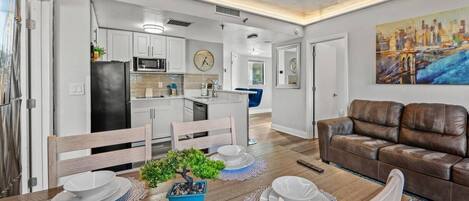 A modern kitchen with white cabinets, a black refrigerator, and a dining area with a wooden table set for four.