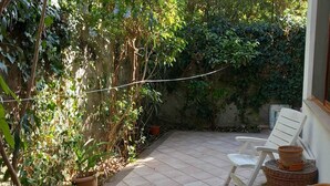 Un patio con piso de baldosas, mobiliario de mimbre y plantas en macetas.