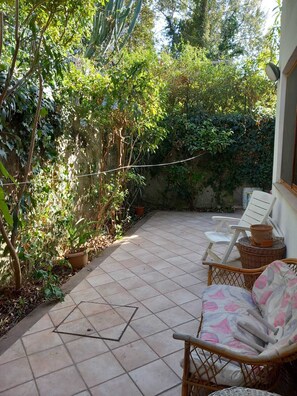 Une terrasse avec un sol carrelé, des meubles en osier et des plantes en pot.