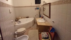 Un baño con bañera, inodoro, bidé, lavabo, espejo y un televisor montado en la pared.