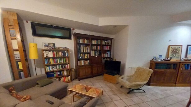 Una sala de estar con sofá, sillón, estantería, televisor y lámpara.