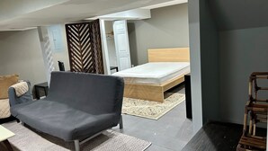 Une chambre à coucher de taille modeste, comprenant un lit simple, un canapé gris, une petite table et un tapis à motifs.