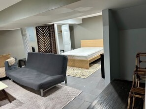 Ein kleines Schlafzimmer mit einem Einzelbett, einem grauen Sofa, einem kleinen Tisch und einem gemusterten Teppich.