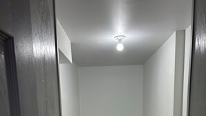 Un couloir étroit avec un luminaire au plafond, des murs blancs et un sol carrelé de couleur grise.