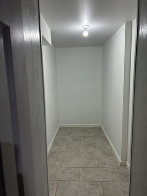 A narrow hallway with a ceiling light, white walls, and grey tiled flooring. - Private office space plus studio vibe bedroom/ living room. Full kitchen W&Dryer (Mableton)