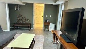 Un salon comprenant un canapé, une table basse, un téléviseur et une porte donnant sur une autre pièce.