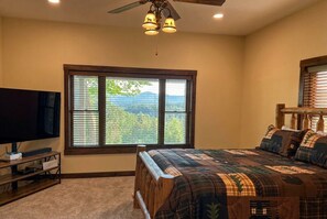 Une chambre à coucher comprenant un lit, un téléviseur, une fenêtre donnant sur la montagne et un ventilateur de plafond.