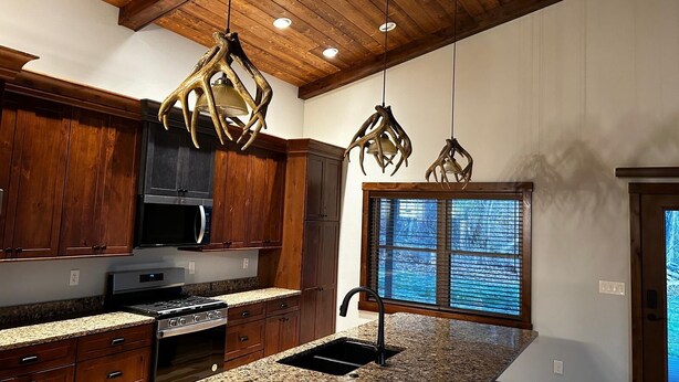 Una cocina con gabinetes de madera, encimeras de granito, una estufa de acero inoxidable y una ventana con persianas.