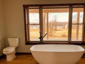 Ein Badezimmer mit einer freistehenden Badewanne, einer Toilette und einem Fenster mit Blick auf ein Feld.
