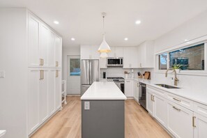 A modern kitchen with white cabinetry, a central island, stainless steel appliances, and a pendant light. - Spacious 4BR North Van Home - Perfect for Groups (North Vancouver)