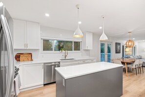 A modern kitchen with white cabinetry, a central island, pendant lighting, and a dining area with a table and chairs. - Spacious 4BR North Van Home - Perfect for Groups (North Vancouver)