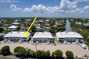 An aerial view of a residential area with a river, houses, and a large building with a flat roof and multiple windows. - Sanibel Arms A8- Gorgeous Condo Steps to Beach (Sanibel)