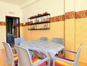 Un coin repas comprenant une table ronde, six chaises et une étagère murale où sont rangés les ustensiles de cuisine.