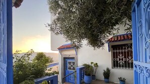 Ein Innenhof mit einem blauen Tor, Blumentöpfen und Blick auf den Sonnenuntergang.