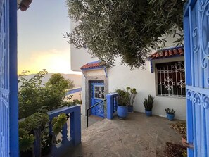 Ein Innenhof mit einem blauen Tor, Blumentöpfen und Blick auf den Sonnenuntergang.